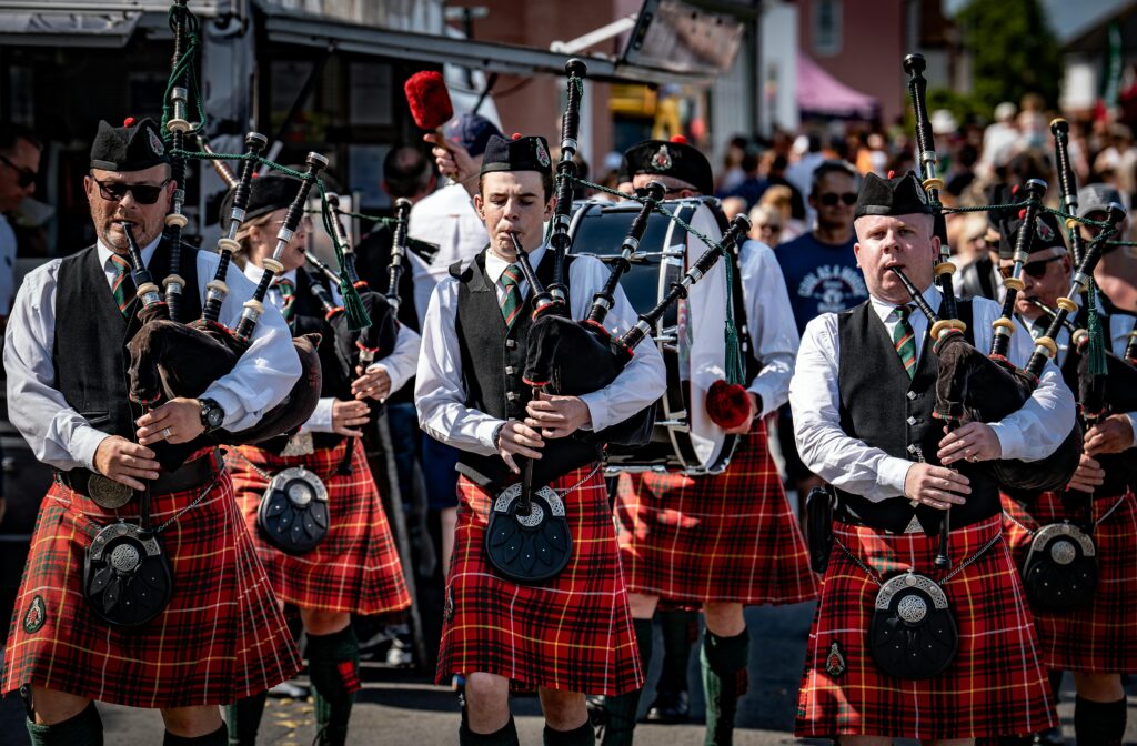 pexels-photo-33660210-33660210 Traditional Scottish bagpipers in kilts performing at a lively outdoor event in the UK.