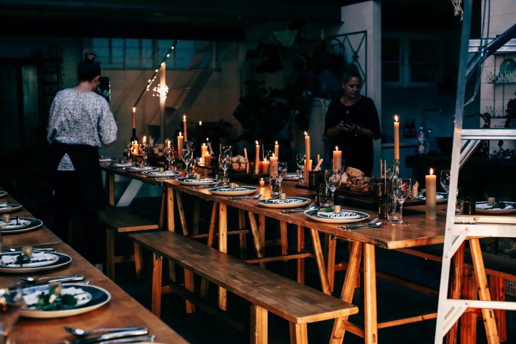 pexels-photo-4992830-4992830 Anonymous women serving wooden tables with plates and glassware among burning candles while preparing for banquet in modern place